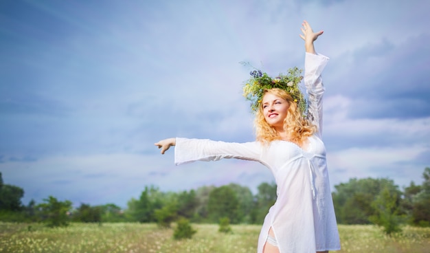 Jonge mooie blonde vrouw in witte kleding en kroon die zich met gesloten ogen bevinden en van zonneschijn op de zomerdag genieten