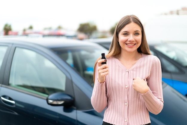 Jonge mooie blonde vrouw met autosleutels buitenshuis met verrassende gelaatsuitdrukking