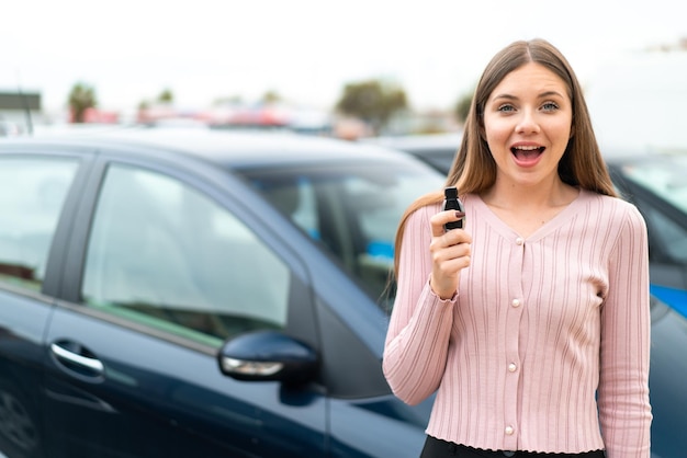 Jonge mooie blonde vrouw met autosleutels buitenshuis met verrassing en geschokte gezichtsuitdrukking