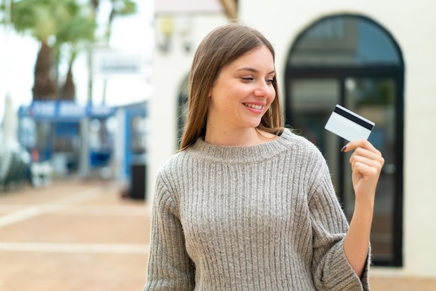 Jonge mooie blonde vrouw met een creditcard buitenshuis met een gelukkige uitdrukking