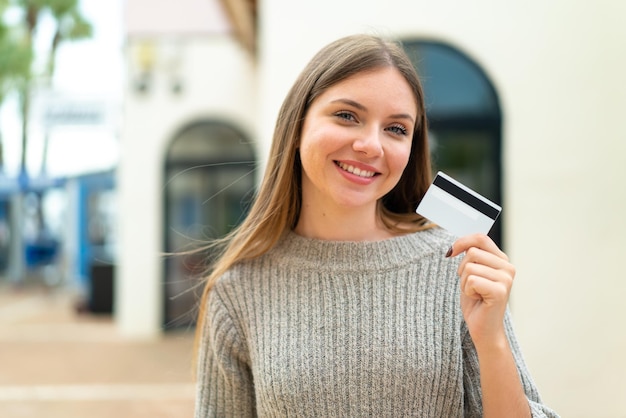 Jonge mooie blonde vrouw met een creditcard buitenshuis veel lachend