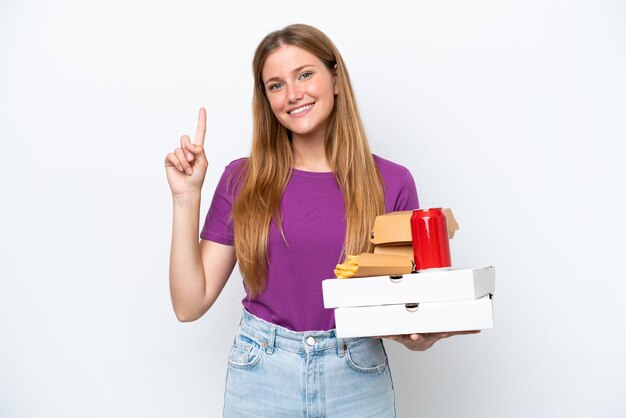 Jonge mooie blonde vrouw met fastfood geïsoleerd op een witte achtergrond die een vinger toont en opheft als teken van het beste