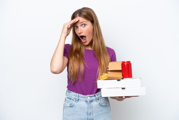 Jonge mooie blonde vrouw met fastfood geïsoleerd op een witte achtergrond die verrassingsgebaar doet terwijl ze naar de zijkant kijkt