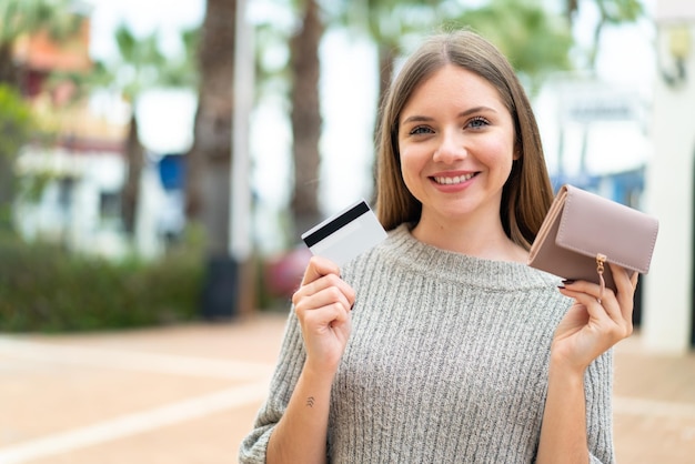 Jonge mooie blonde vrouw met portemonnee en creditcard met gelukkige uitdrukking