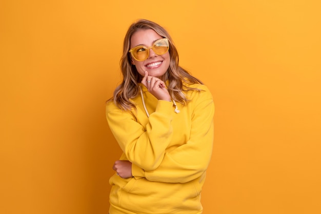 Jonge mooie blonde vrouw schattige gezichtsuitdrukking poseren in gele hoodie op geel helder geïsoleerd