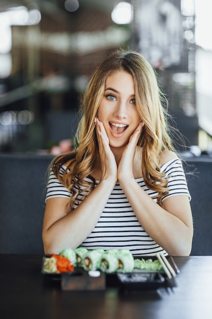 Jonge mooie blonde vrouw sushi eten op het zomerterras van een japans restaurant?