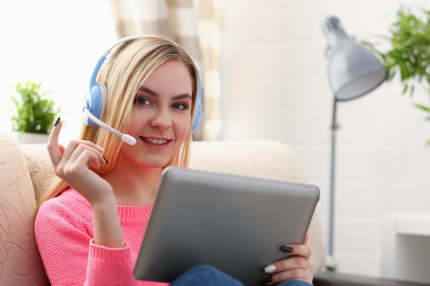jonge mooie blonde vrouw zitten op de bank in de woonkamer tablet houden in armen luisteren naar zonnige muziek