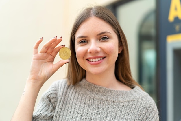 Jonge mooie blondevrouw die een Bitcoin met gelukkige uitdrukking houdt