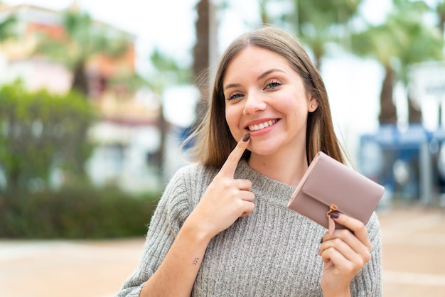 Jonge mooie blondevrouw die een portefeuille met gelukkige uitdrukking houdt