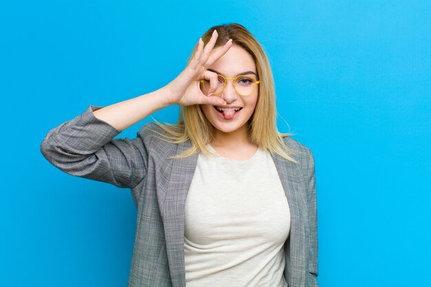 Jonge mooie blondevrouw die gelukkig met grappig gezicht glimlachen