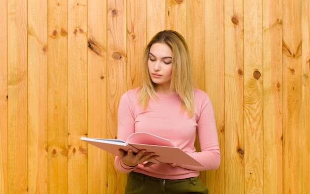 Jonge mooie blondevrouw met boeken houten muur