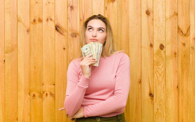 Jonge mooie blondevrouw met dollarbankbiljetten tegen houten muur