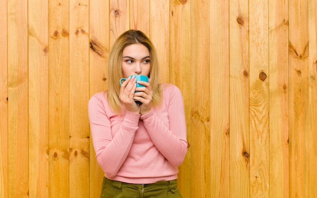 Jonge mooie blondevrouw met een koffiekop tegen houten muur