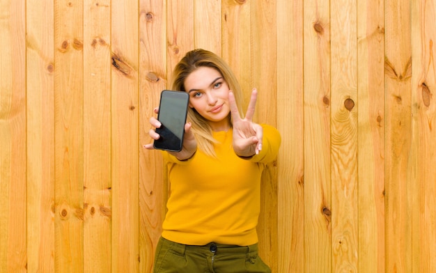 Jonge mooie blondevrouw met een mobiele telefoon tegen houten muur