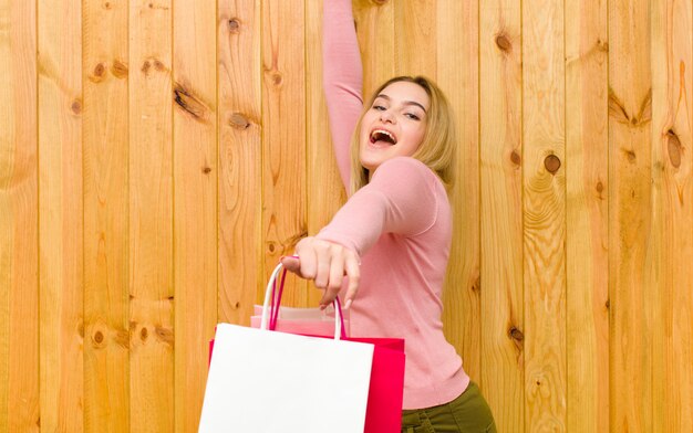 Jonge mooie blondevrouw met het winkelen zakken tegen houten muur