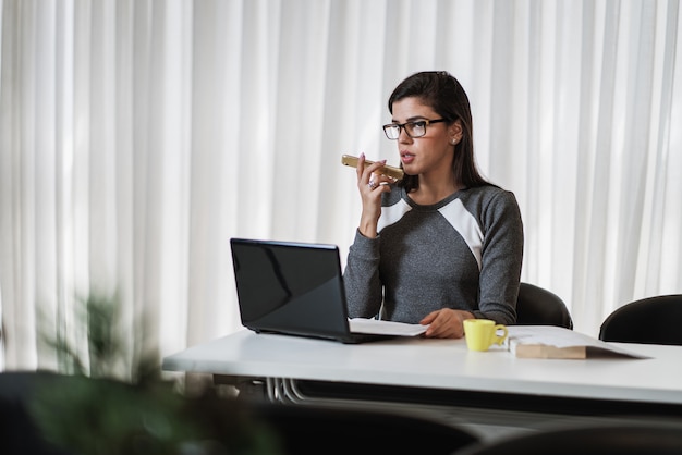 Jonge mooie Braziliaanse vrouw die smartphone gebruikt en met laptop werkt