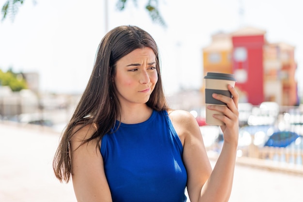 Jonge mooie Braziliaanse vrouw met een afhaalkoffie buitenshuis met droevige uitdrukking