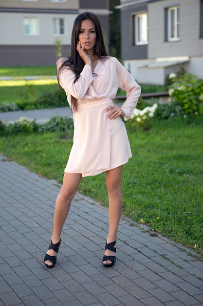 Jonge mooie brunette in een lichte zomerjurk poseren op straat