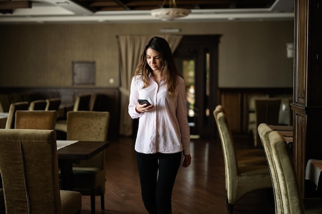 Jonge mooie brunette vrouw lopen in restaurant en kijken naar de telefoon