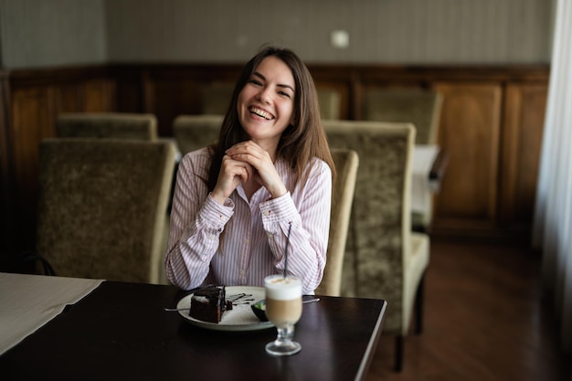Jonge mooie brunette vrouw zit binnen in het café-restaurant van de coffeeshop en lacht