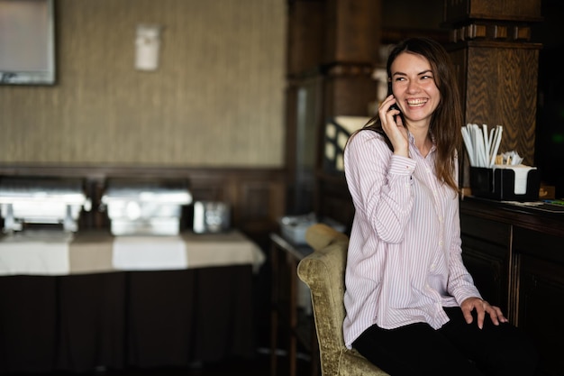 Jonge mooie brunette vrouw zitten in de buurt van toog praten aan de telefoon en lachen