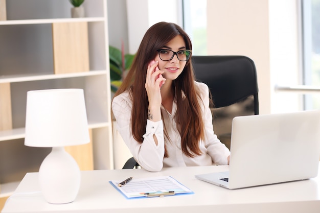 Jonge mooie brunette zakelijke vrouw met laptop op kantoor.