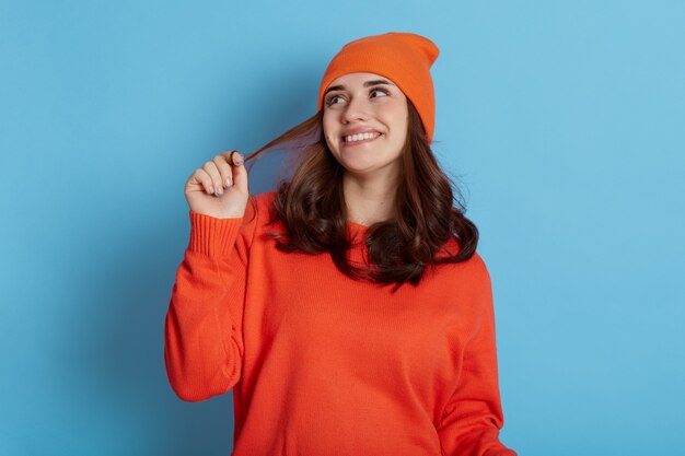 Foto jonge mooie dame kijkt dromerig opzij, glimlachend gelukkig geïsoleerd op blauw, haar haren opzij te trekken