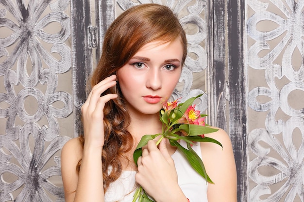 Jonge mooie dame met bloemen op grijze achtergrond. Huidverzorgingsconcept. Portret van een jong lief meisje in de studio op een grijze achtergrond met een groene bloem in de hand