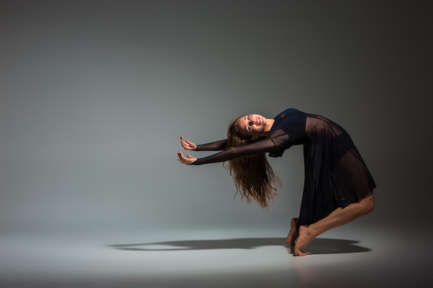 Jonge mooie danseres in zwarte jurk poseren op een donkergrijze studio achtergrond. Modern, Hedendaags, improvisatie