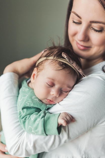 Jonge mooie donkerharige moeder houdt haar pasgeboren dochter in haar armen in een gezellig huis Familieportret Moederschap Jonge vrouw kust haar 2 maanden oude baby