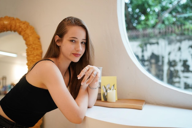 Jonge mooie en aantrekkelijke vrouw met lang bruin haar in een zwarte jurk in café tegen stedelijke achtergrond.