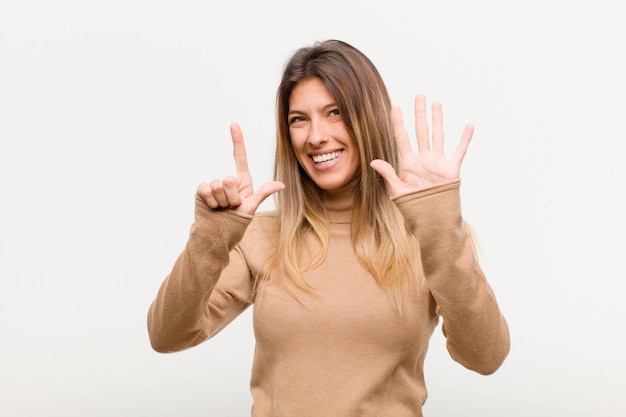 Jonge mooie en vrouw die vriendelijk glimlachen kijken, nummer zeven of zevende met vooruit hand tonen, die tegen witte muur aftellen