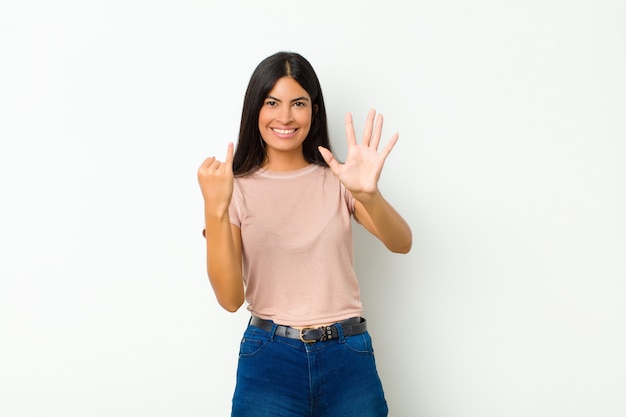 Jonge mooie en vrouw die vriendelijk glimlachen kijken, tonend nummer zes of zesde met voorwaartse hand, aftellend over muur