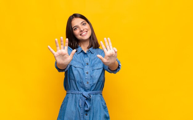 Jonge mooie en vrouw die vriendelijk glimlacht kijkt, nummer negen of negende met vooruit hand toont, aftellend