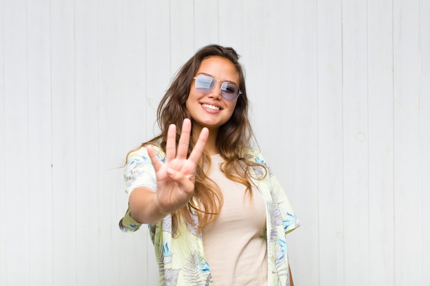 Jonge mooie en vrouw die vriendelijk glimlacht kijkt, nummer vier of vierde met vooruit hand toont, aftellend