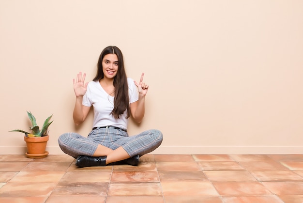 Jonge mooie en vrouw die vriendelijk glimlacht kijkt, nummer zeven of zevende met vooruit hand toont, die zitting op een vloer aftelt