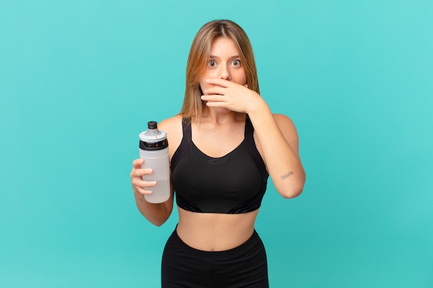 Jonge mooie fitness vrouw die mond bedekt met handen met een geschokt