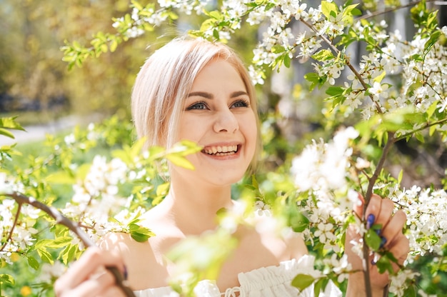 Jonge mooie gelukkig lachende blonde vrouw poseren in bloeiende lentetuin met witte bloemen