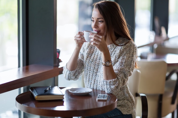 Jonge mooie gelukkige vrouw die koffie drinkt in restaurant