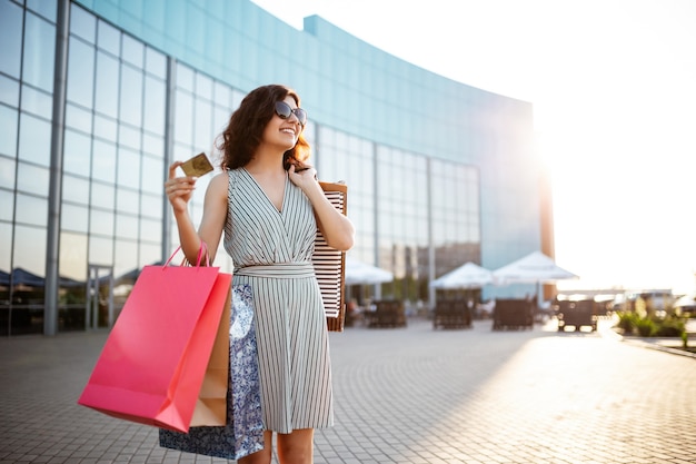 Jonge mooie gelukkige vrouw loopt uit winkelcentrum met aankopen.