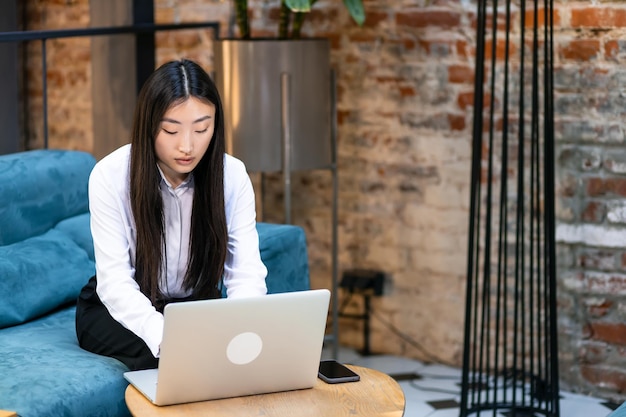 Jonge, mooie glimlachende Aziatische zakenvrouw die aan een laptop werkt, gehuisvest aan een houten tafel in kantoor