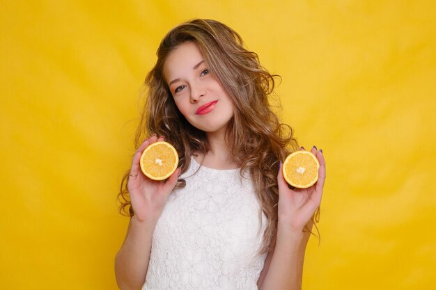 Jonge mooie grappige mannequin met sinaasappelschijfje op oranje achtergrond. met make-up en kapsel. met citroen met een mooie glimlach.