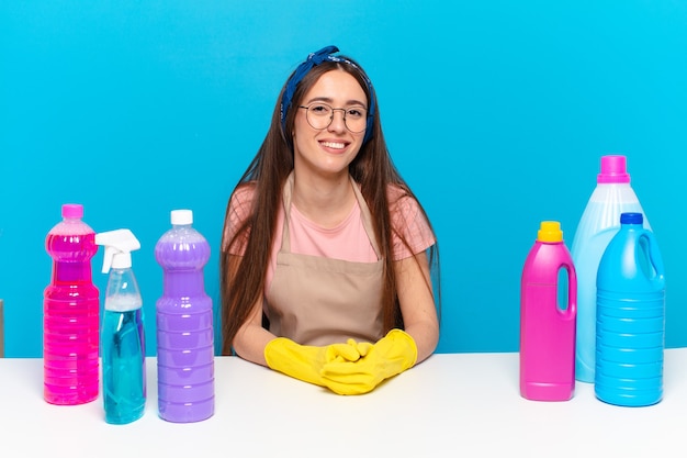 Jonge mooie huisbewaarder die gelukkig glimlacht met een hand op heup en zelfverzekerde, positieve, trotse en vriendelijke houding