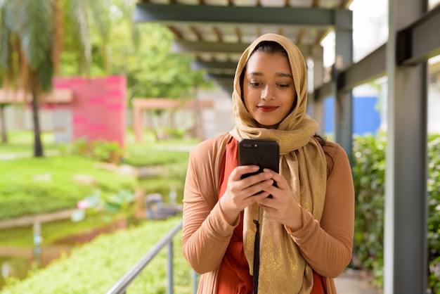 Jonge mooie Indiase moslimvrouw met behulp van telefoon in het park