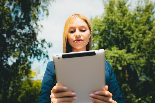 Jonge mooie Kaukasische meisje met behulp van mobiele tablet in het park in de zomer