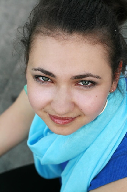 Jonge mooie krullend brunette meisje met een blauwe sjaal zittend in het park en kijken naar de camera