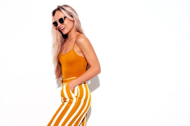 Jonge mooie lachende blonde vrouw in trendy zomer gele kleding Sexy zorgeloze vrouw geïsoleerd op wit in studio Positief model plezier binnenshuis vrolijk en gelukkig In zonnebril