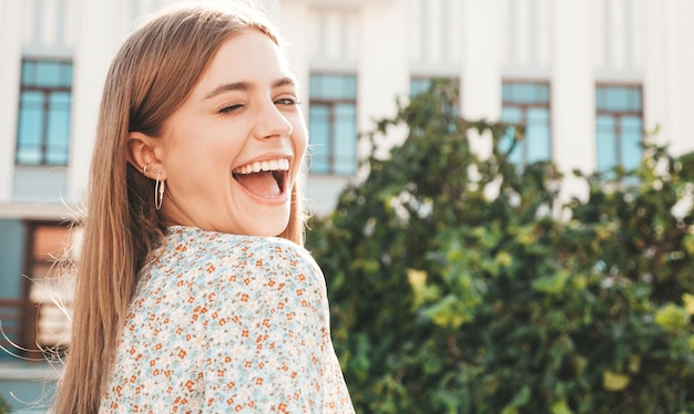 Jonge mooie lachende hipster vrouw in trendy zomerjurk Sexy zorgeloze vrouw die zich voordeed op de straat achtergrond bij zonsondergang Positief model buitenshuis vrolijk en gelukkig Winking