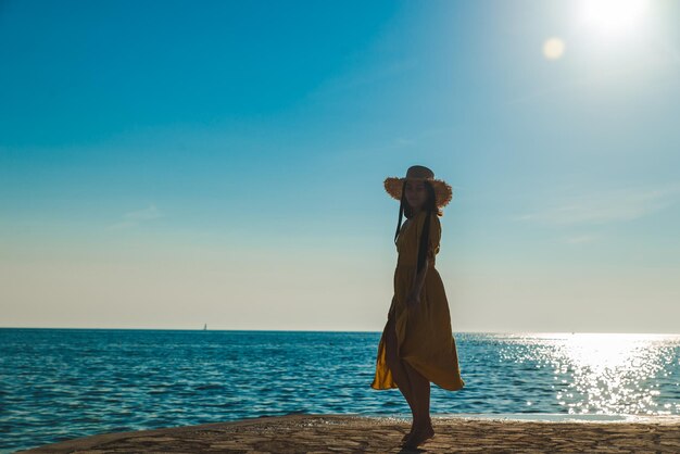 Jonge mooie lachende vrouw in gele zomerjurk wandelen door stenen strand
