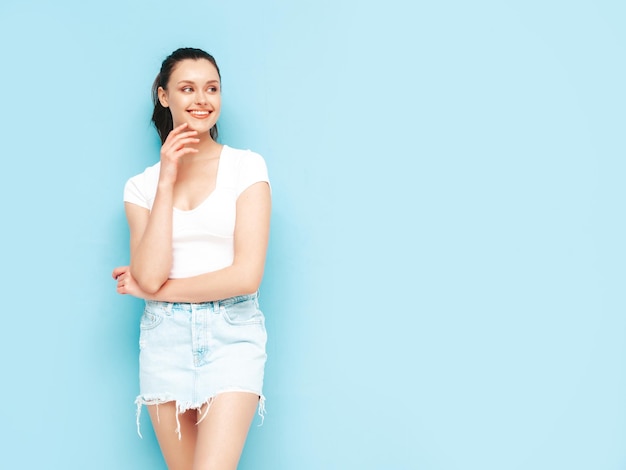 Jonge mooie lachende vrouw in trendy zomer jeans rok en top kleding Sexy zorgeloze vrouw poseren in de buurt van blauwe muur in studio Positieve brunette model plezier vrolijk en gelukkig